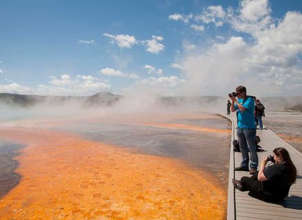 students stand on boardwalk above orange pools at yellowstone