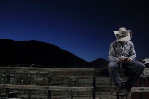 cowboy sitting on a fence at twilight