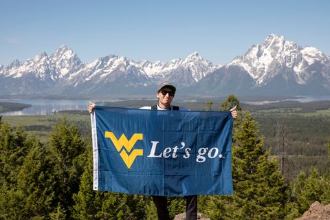 student holds WVU flag in front of rocky mountains